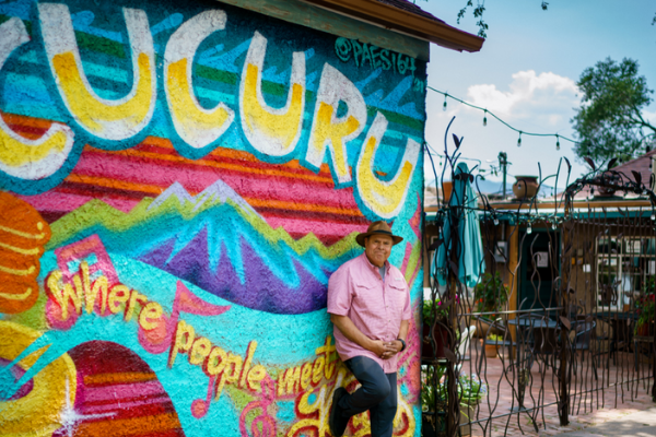 Cafe owner stands in front of colorful mural near dining patio.